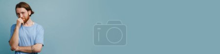 Téléchargez les photos : Jeune homme roux avec barbe souriante et regardant la caméra isolée sur fond bleu - en image libre de droit