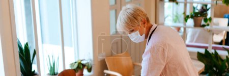 Photo for Mature woman wearing face mask using measuring tape while working in cafe - Royalty Free Image
