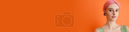 Téléchargez les photos : Jeune femme blanche aux cheveux roses posant et regardant la caméra isolée sur fond orange - en image libre de droit