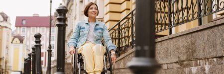 Photo for Brunette woman smiling and sitting in wheelchair on city street - Royalty Free Image