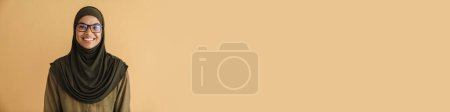Téléchargez les photos : Femme musulmane noire en hijab souriant et regardant la caméra isolée sur fond beige - en image libre de droit
