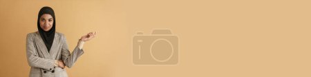Téléchargez les photos : Femme musulmane noire en hijab souriant et tenant copyspace isolé sur fond beige - en image libre de droit