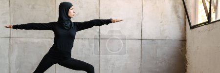 Téléchargez les photos : Jeune femme musulmane en hijab faire de l'exercice pendant la pratique du yoga à l'intérieur - en image libre de droit