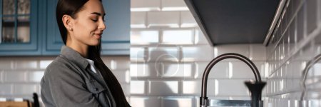 Téléchargez les photos : Heureuse femme brune d'âge moyen qui lave des fruits dans un évier dans la cuisine à la maison - en image libre de droit