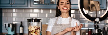 Téléchargez les photos : Rire femme faire smoothie tout en prenant des images selfie sur téléphone portable à la maison cuisine - en image libre de droit