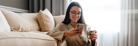 Téléchargez les photos : Femme blanche buvant du thé et utilisant un téléphone portable assis sur le sol à la maison - en image libre de droit