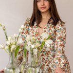 Pretty young woman in dress with flowers and dark hair posing in the room full of flowers