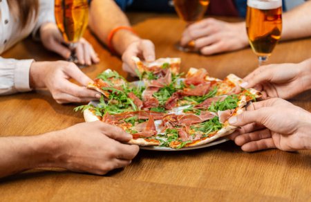 leisure, food and drinks, people and holidays concept - close up of friends eating pizza and drinking beer at restaurant or pub