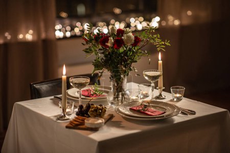 Feiertage, romantisches Datums- und Festkonzept - Nahaufnahme der Festtafel für zwei Personen mit Blumen in der Vase und Kerzen, die am Valentinstag zu Hause brennen