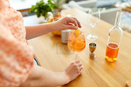 Getränke- und Personenkonzept - Nahaufnahme einer Frau, die in der heimischen Küche Orangencocktail im Weinglas zubereitet