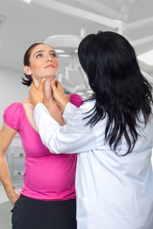 Téléchargez les photos : Docteur endocrinologue vérifiant tyroïde goitre de la femme enceinte et tenant la main sur sa gorge - en image libre de droit