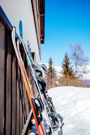 Photo for Skies and snowboard stand on alpine resort near building hotel or home waiting to go on the slope - Royalty Free Image