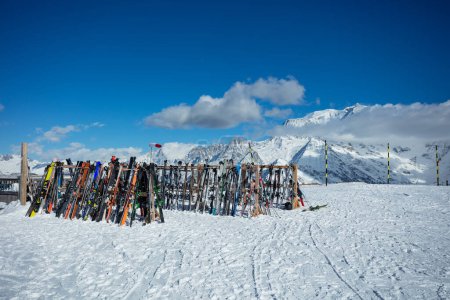 Photo for Large number of skies and snowboards stand on alpine resort near cafe or restaurant over mountain summits on background - Royalty Free Image