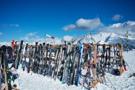 Téléchargez les photos : Large group skis stand on alpine resort near cafe or restaurant over mountain summits on background - en image libre de droit