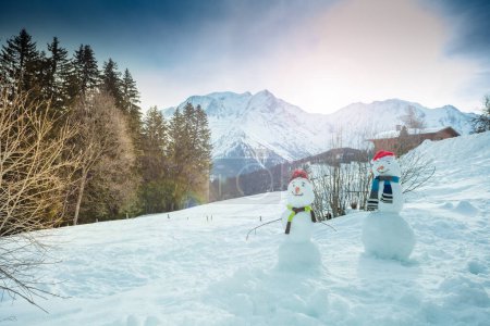 Photo for Snowmen build on the mountain plain on winter vacation with scarf, hat, carrot nose in sunny day - Royalty Free Image