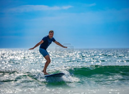 Photo for Man learns to surf on the surfboard balancing getting used to standing on the board on small waves - Royalty Free Image