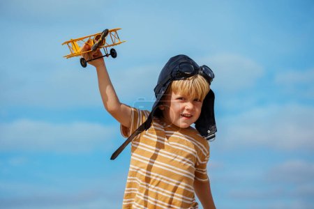 Smiling boy run with toy model of the plane wearing aviation hat and googles on the beach