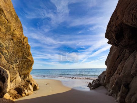 Foto de View of the sea from the cave entrance with rocks on by the side to the sand beach on sunny hot day - Imagen libre de derechos