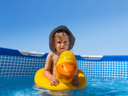 Photo for Little boy in the pool swim in inflatable duck playing in the water and smiling - Royalty Free Image