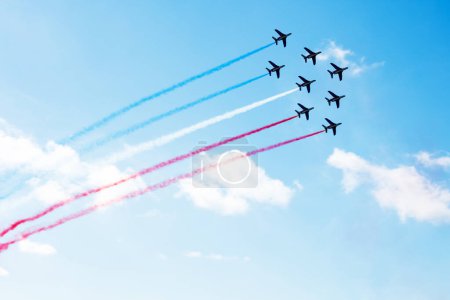 Foto de Squadron of planes fly with color trail in blue red white lines over clouds and clear sky in colors of USA Holland or France - Imagen libre de derechos