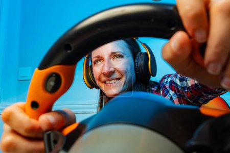 Photo for Portrait through the console steering wheel of a gamer woman in headphones playing race game - Royalty Free Image