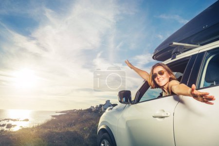 Foto de Retrato de una mujer en la ventana del coche relajado estiramiento y agitar las manos sonriendo, con gafas de sol - Imagen libre de derechos