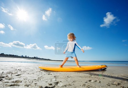 Photo for Profile portrait of a cute blond girl train standing on the surfboard learning balance practicing surfing before going to ocean, view over sun - Royalty Free Image