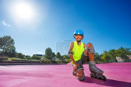 Photo for Happy preteen boy sit and pose in blue helmet with rollerblades in the skatepark wearing protection - Royalty Free Image