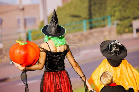 Téléchargez les photos : Famille de la mère et le groupe d'enfants garçons, les filles en costumes déguisés Halloween tenir énorme promenade citrouille, vue de près par derrière - en image libre de droit