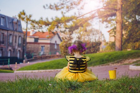 Foto de Happy little girl in Halloween bee costume disguise sit with small bucket for candies view from behind - Imagen libre de derechos