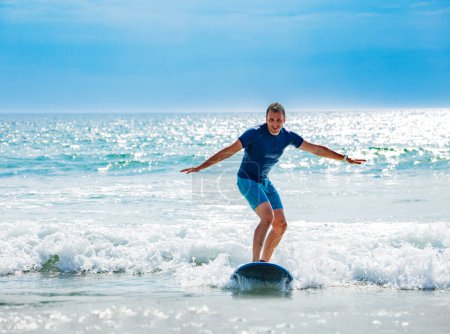 Photo for Man learns to surf the wave on the surfboard balancing getting used to standing on the board on small waves - Royalty Free Image