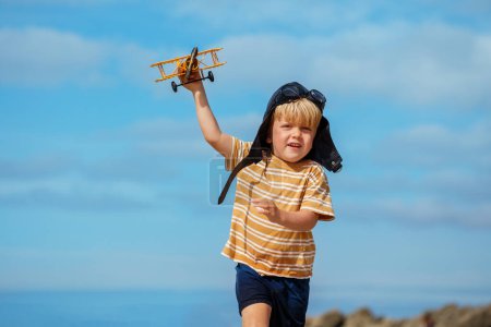 Foto de Retrato cercano de un niño con modelo de juguete del avión con sombrero de aviación y googles en la playa - Imagen libre de derechos