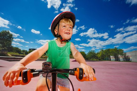 Photo for W low angle portrait of a little blond smiling boy ride small bicycle on color surface of the park - Royalty Free Image