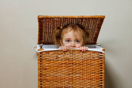 Retrato de una hermosa niña está jugando alegremente un juego de escondite, asomándose desde una caja de ropa de madera.