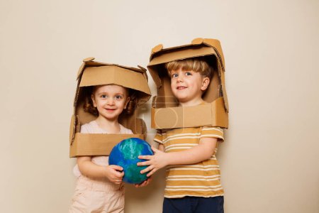 Foto de Felices hermanos niño y niña se mantienen unidos planeta tierra en cartulina astronautas cascos de bricolaje - Imagen libre de derechos