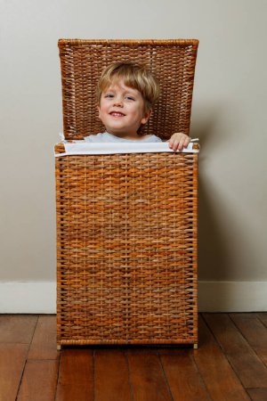 Foto de El niño pequeño está jugando alegremente un juego de escondite, asomándose de una caja de ropa de madera. - Imagen libre de derechos
