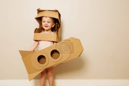Foto de Feliz niña sonriente en casco de cartón con cohete hecho en las manos - Imagen libre de derechos