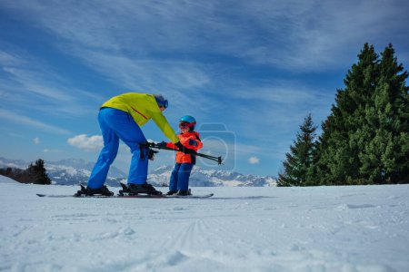 Photo for Adult on skiing slope glide backwards teaching little child to ski going downhill holding poles in hands - Royalty Free Image