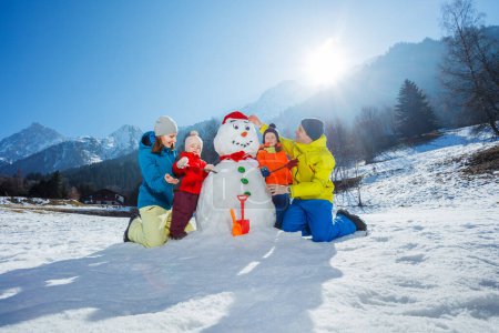 Photo for Happy mom dad and two little kids boy with girl build together snowman in mountains - Royalty Free Image