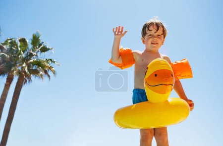 Photo for Cute boy waving hands standing with yellow dusk ring and arm bands over blue sky - Royalty Free Image
