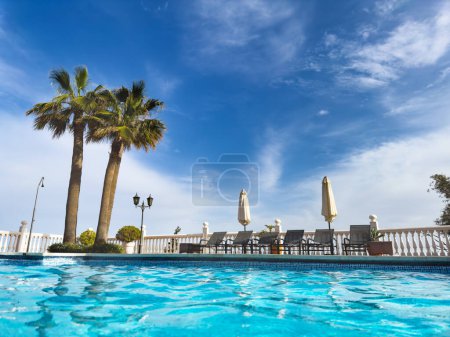 Foto de Vista de ángulo bajo de una piscina cristalina y chaise longs con palmeras en la frontera - Imagen libre de derechos