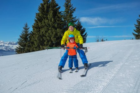 Instructeur enseigne petit enfant glisse de ski derrière tenant bâtons de ski avec les mains montrant le mouvement de coin chasse-neige