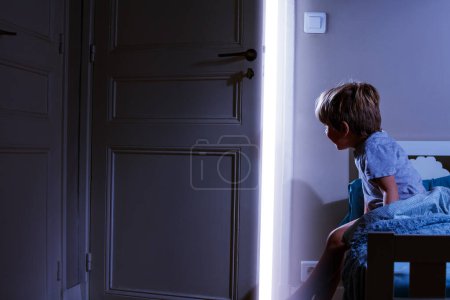 Foto de Niño en el dormitorio mira la luz que viene de la puerta abierta - Imagen libre de derechos