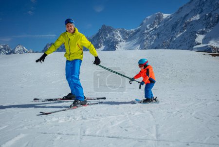 Photo for Instructor on skiing slope glide downhill teaching little child to ski both holding poles - Royalty Free Image