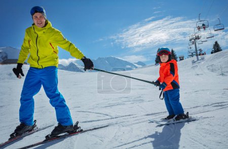 Foto de Padre en la pista de esquí deslizarse cuesta abajo enseñando a los niños a esquiar los dos polos de la celebración - Imagen libre de derechos