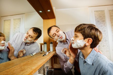Téléchargez les photos : Père et le fils s'amusent dans la salle de bain à se raser en mettant de la mousse sur le visage de l'autre - en image libre de droit