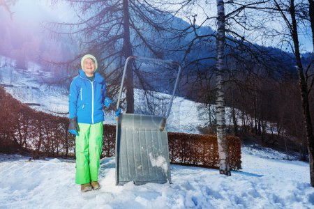 Téléchargez les photos : Support enfant joyeux tenant une grosse pelle pour nettoyer la neige en hiver dans la chaîne de montagnes française - en image libre de droit