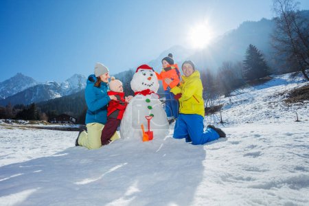 Photo for Happy family of mother father and tow little kids boy with girl build together snowman in mountains - Royalty Free Image