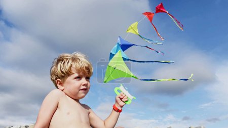 Photo for Close-up of a little boy stand holding many kites in hand smiling over blue sky view from behind - Royalty Free Image