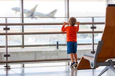 Foto de Niño pequeño de pie cerca de la ventana en el salón del aeropuerto mirando el avión despegar fuera - Imagen libre de derechos